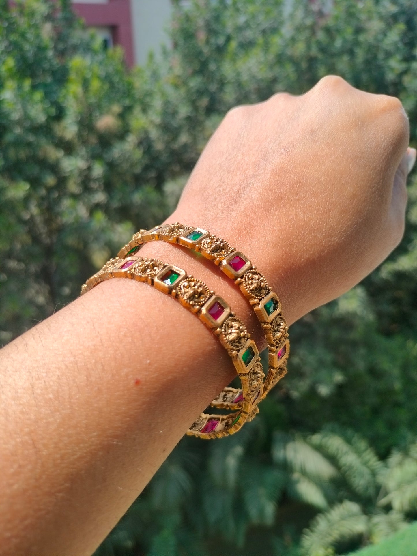 Golden color bangles with gemstones on a wrist against a blurred green background